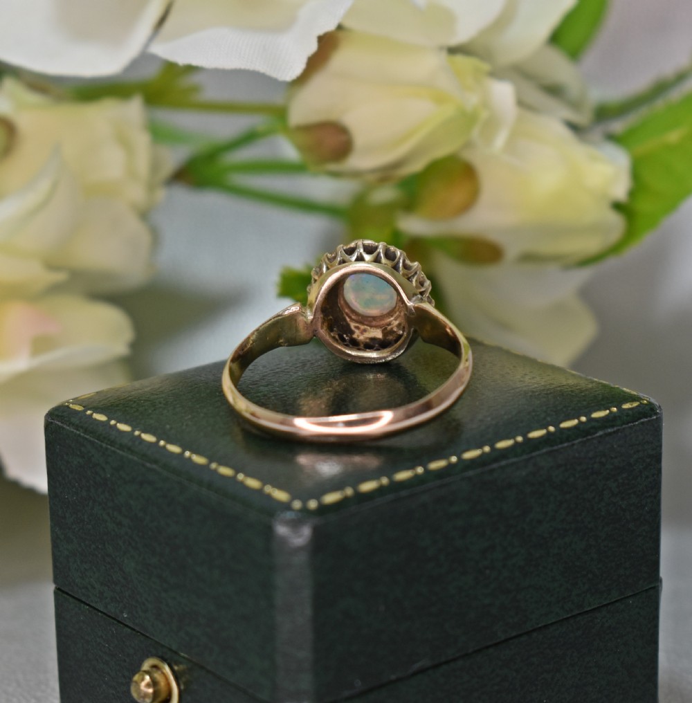 An antique gold Victorian cluster ring featuring a central cabochon opal surrounded by a halo of rose-cut diamonds, displayed inside a green velvet ring box. View VI