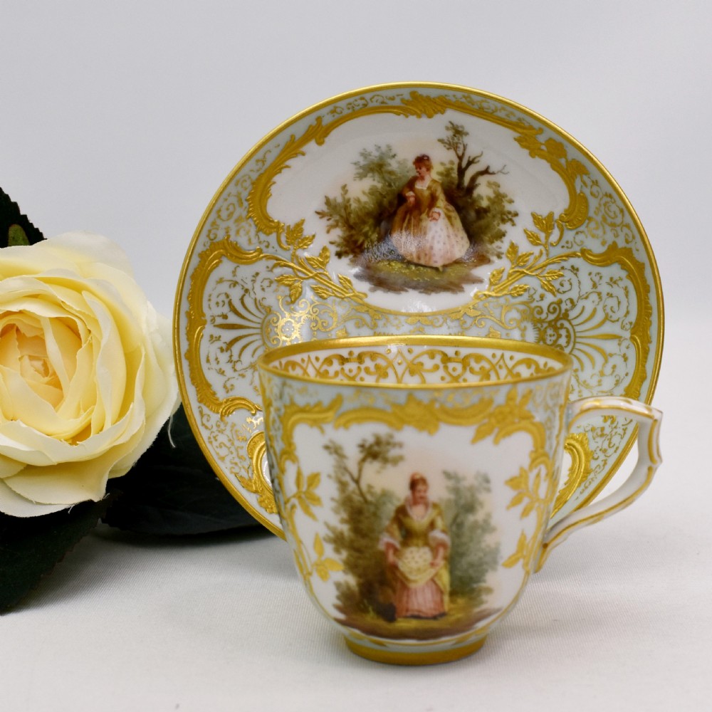 A nineteenth-century KPM Berlin porcelain teacup and matching saucer featuring gilded relief scrollwork and hand-painted figures in a landscape.