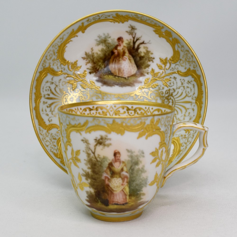 A nineteenth-century KPM Berlin porcelain teacup and matching saucer featuring gilded relief scrollwork and hand-painted figures in a landscape. View II