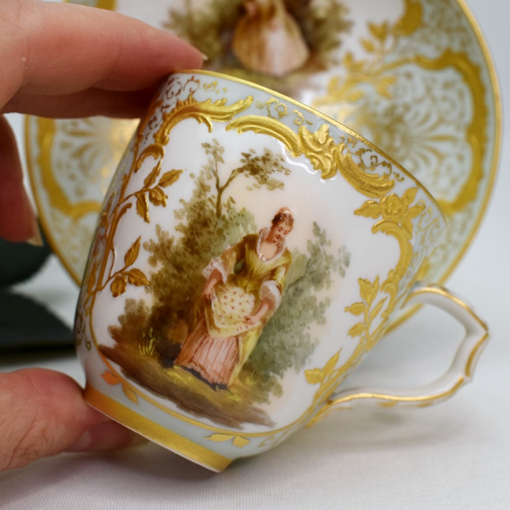 A nineteenth-century KPM Berlin porcelain teacup and matching saucer featuring gilded relief scrollwork and hand-painted figures in a landscape. View III