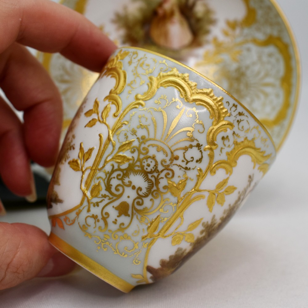 A nineteenth-century KPM Berlin porcelain teacup and matching saucer featuring gilded relief scrollwork and hand-painted figures in a landscape. View V