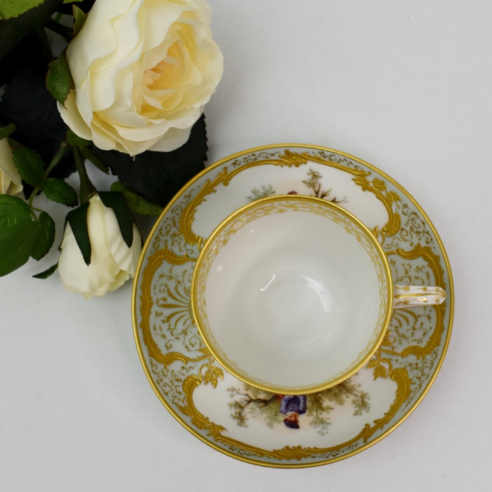 A nineteenth-century KPM Berlin porcelain teacup and matching saucer featuring gilded relief scrollwork and hand-painted figures in a landscape. View X
