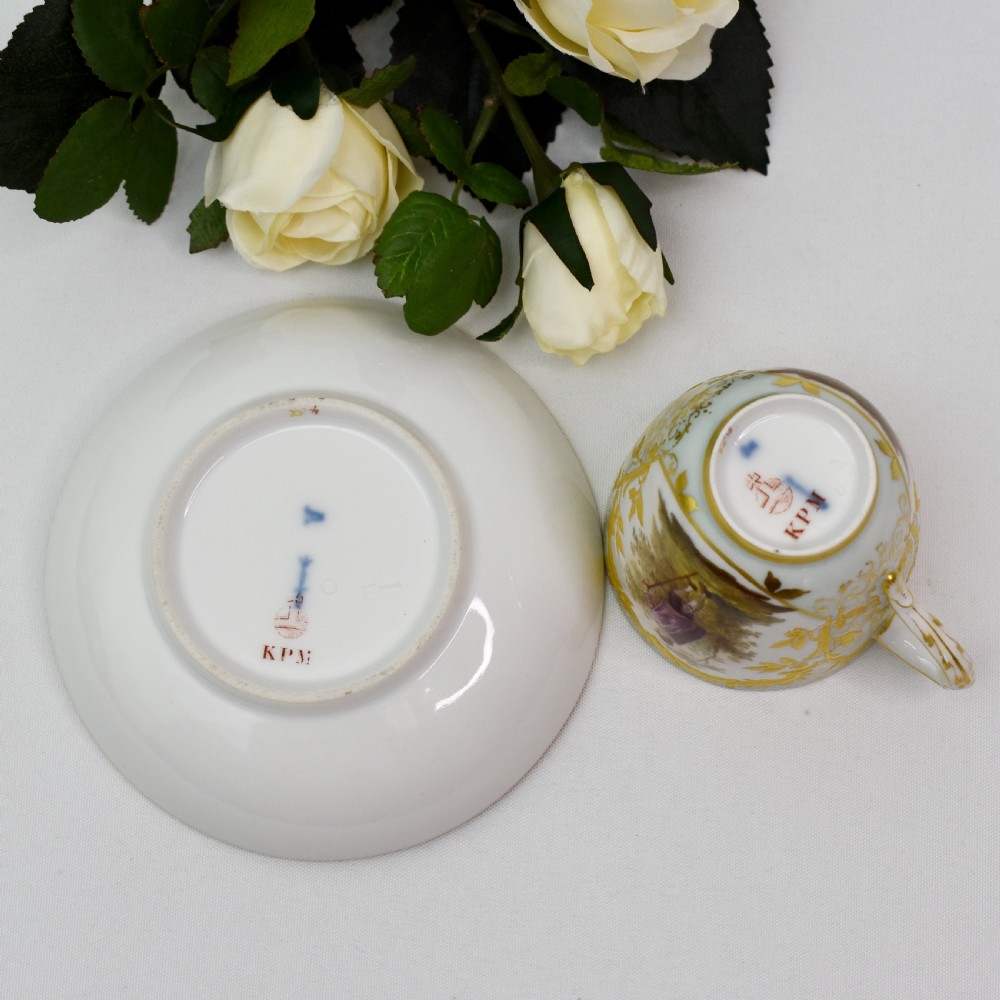 A nineteenth-century KPM Berlin porcelain teacup and matching saucer featuring gilded relief scrollwork and hand-painted figures in a landscape. View XIII