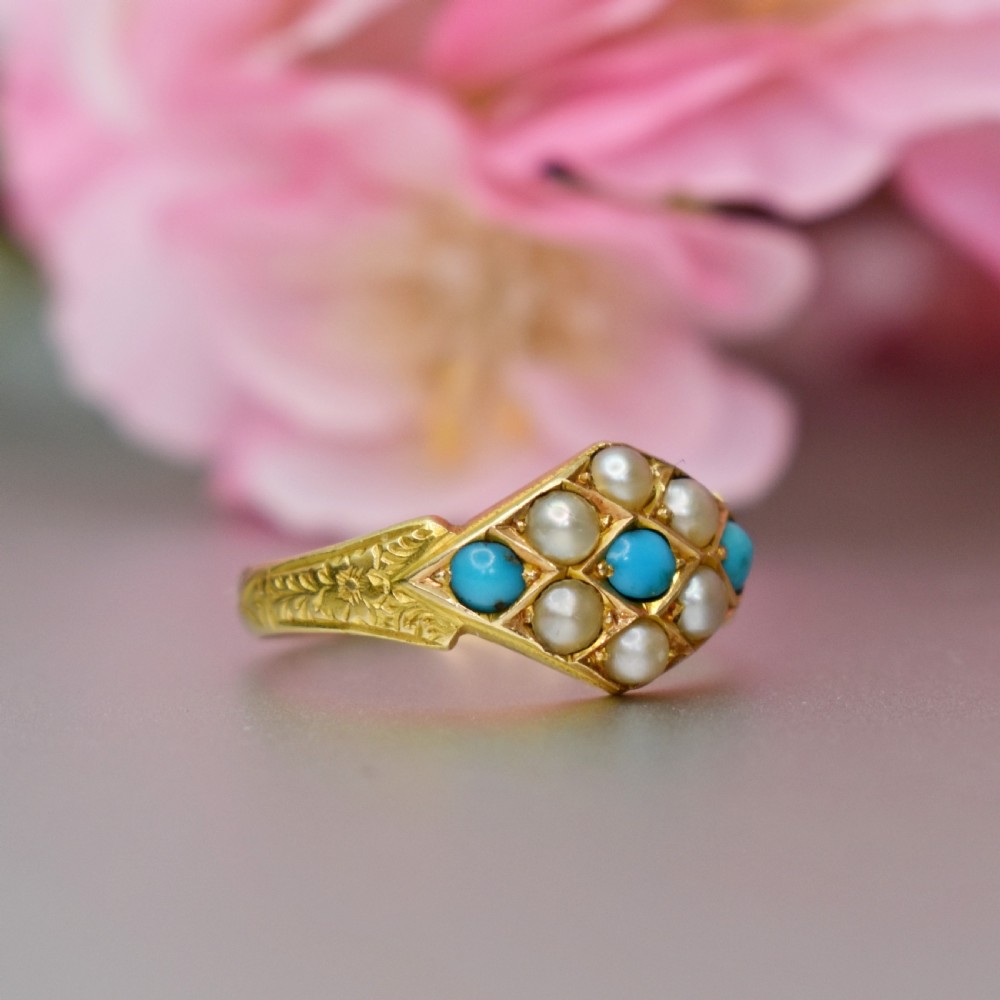 A late Victorian 15ct yellow gold ring featuring a diamond-shaped face set with turquoise cabochons and split pearls, flanked by engraved shoulders.