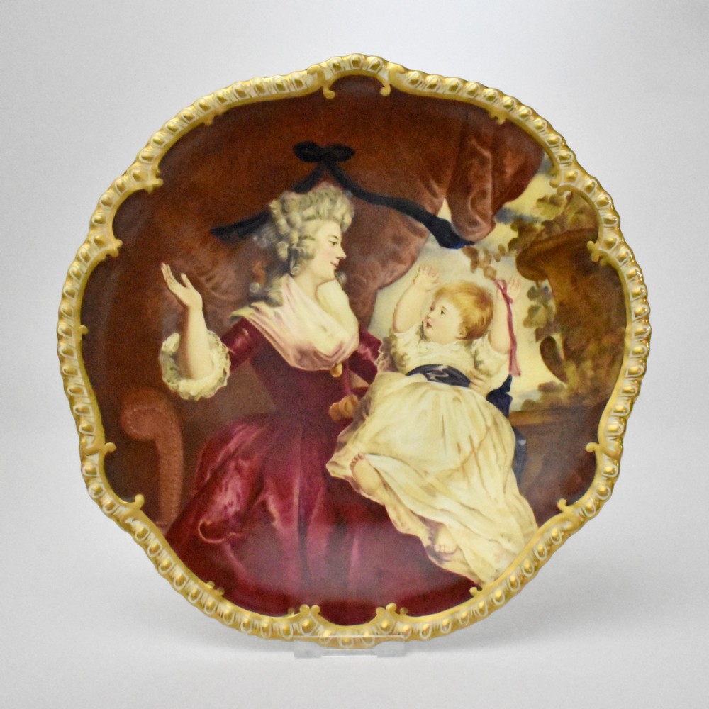 An Edwardian Coalport porcelain cabinet plate featuring a hand-painted portrait of a lady and child within a gold gilded scalloped rim.