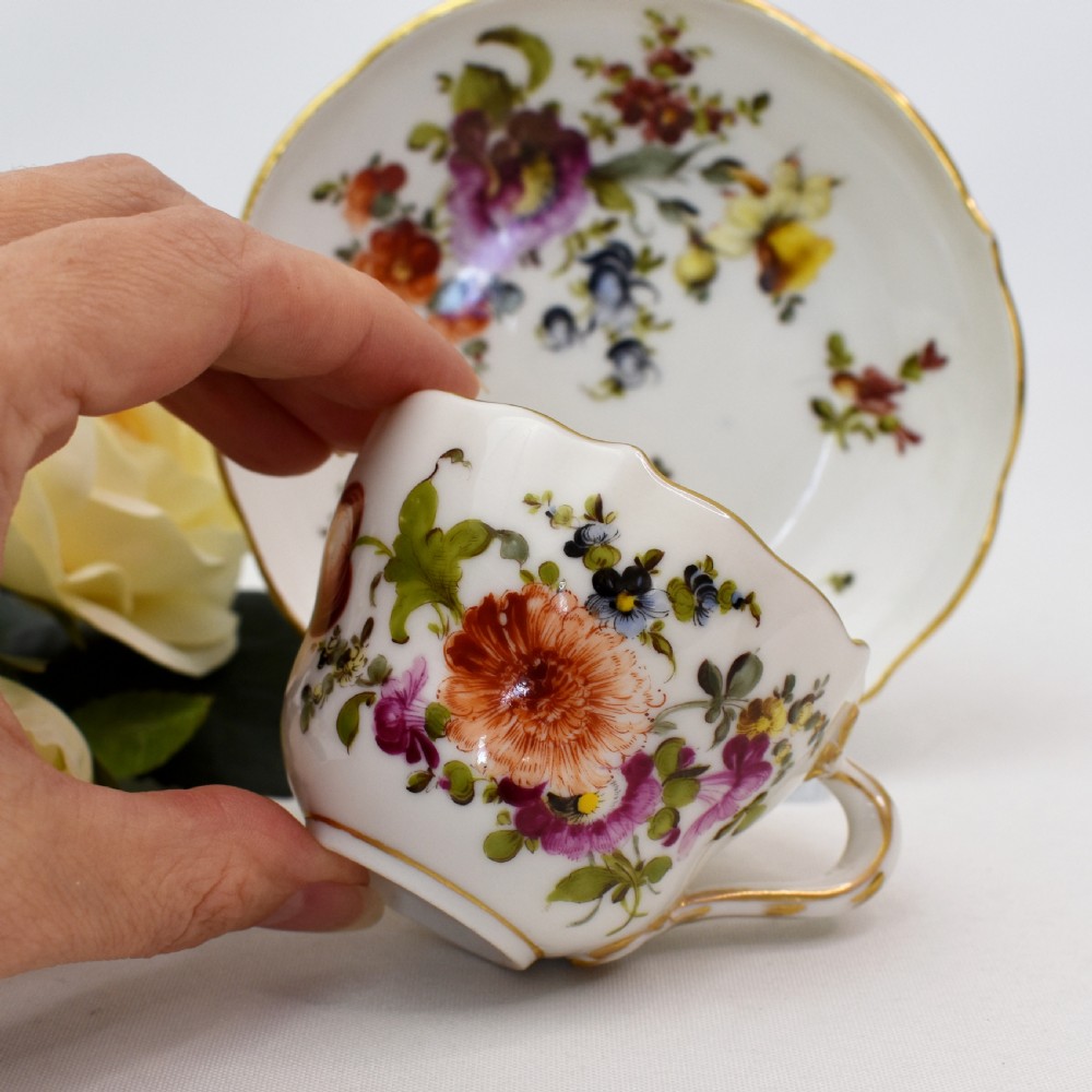 A white porcelain demitasse cup and matching saucer painted with polychrome floral sprays and finished with gold gilded scalloped edges. View III