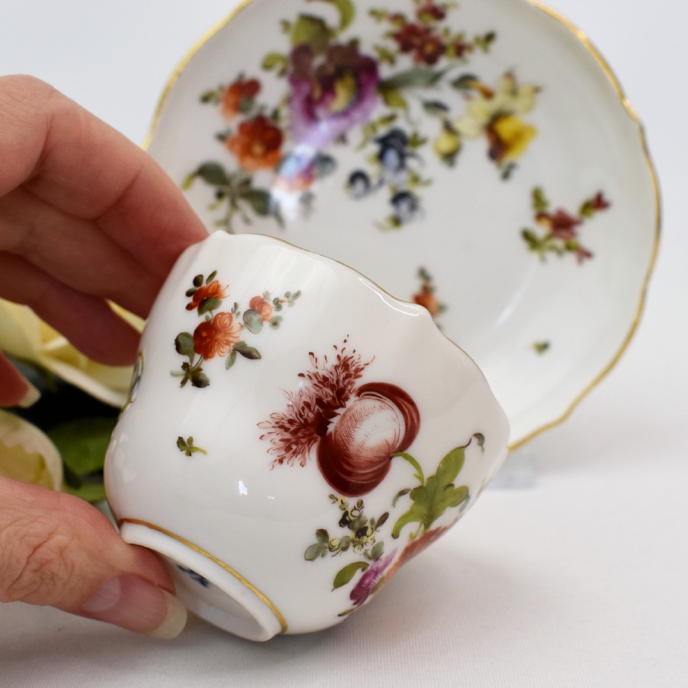A white porcelain demitasse cup and matching saucer painted with polychrome floral sprays and finished with gold gilded scalloped edges. View V