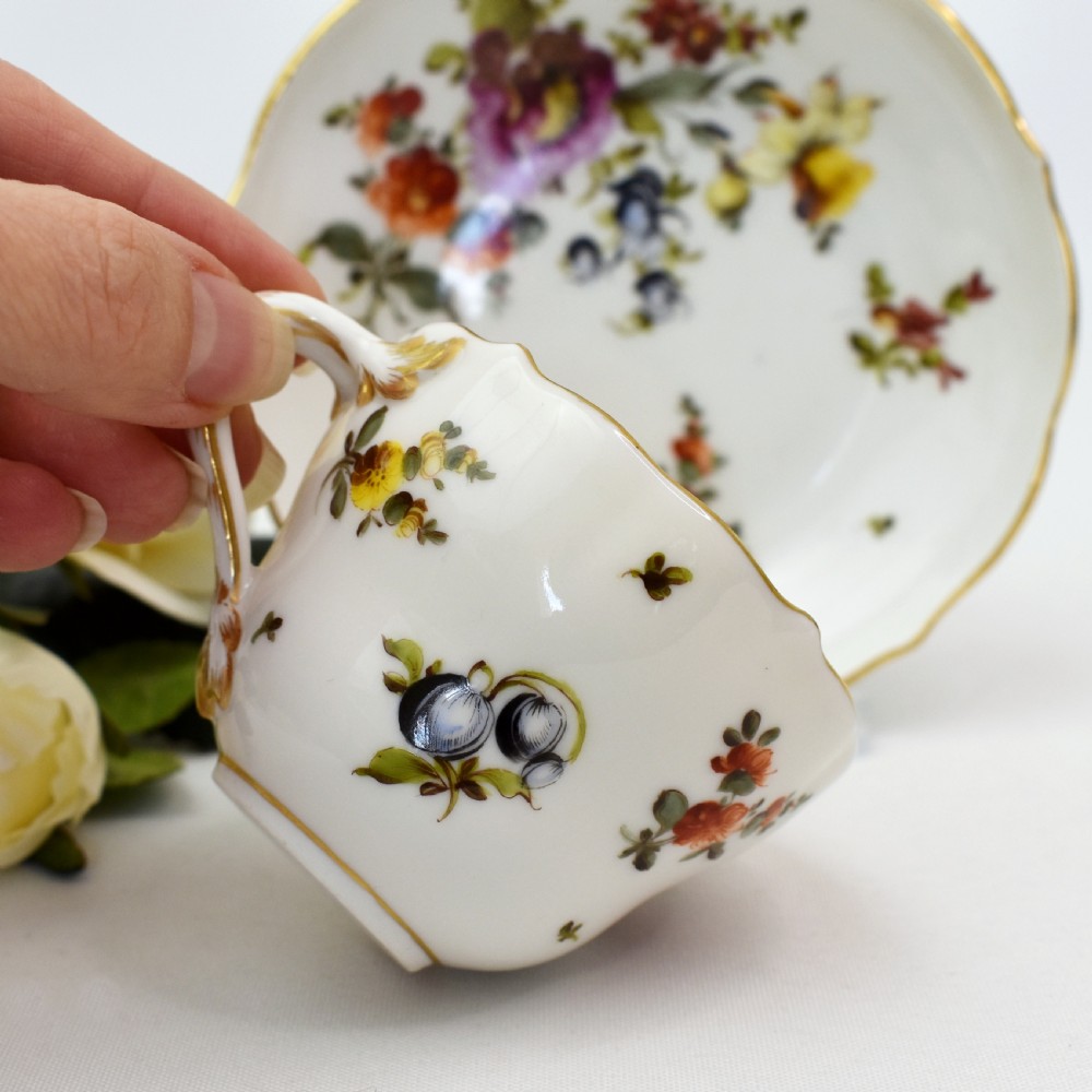 A white porcelain demitasse cup and matching saucer painted with polychrome floral sprays and finished with gold gilded scalloped edges. View VI