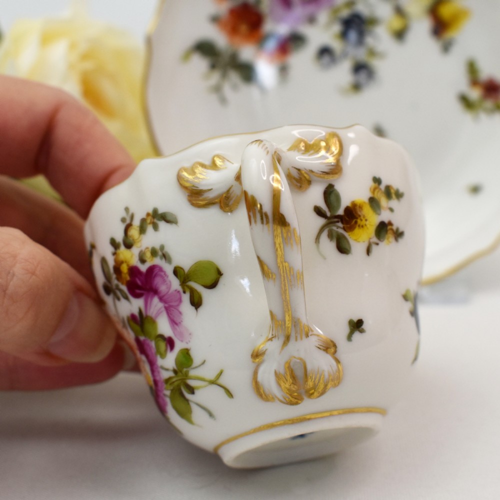 A white porcelain demitasse cup and matching saucer painted with polychrome floral sprays and finished with gold gilded scalloped edges. View VII