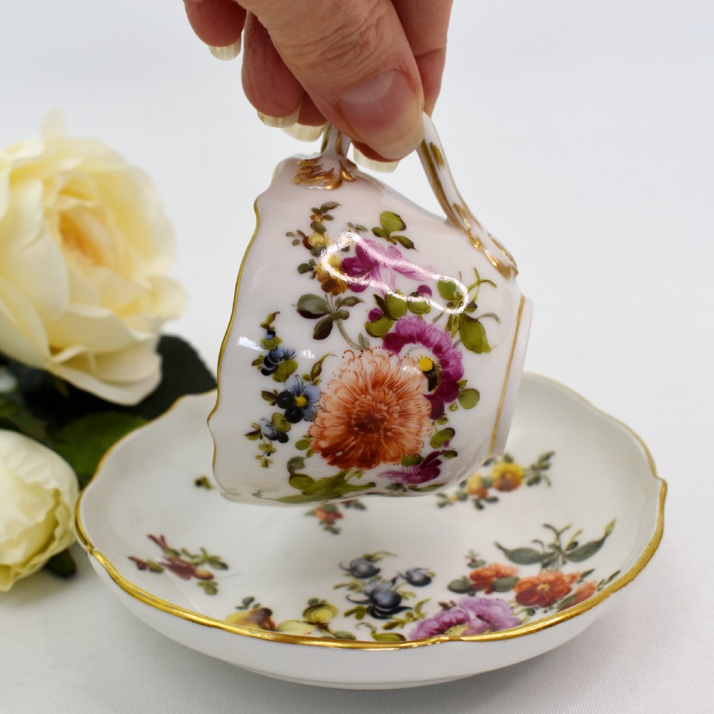 A white porcelain demitasse cup and matching saucer painted with polychrome floral sprays and finished with gold gilded scalloped edges. View VIII