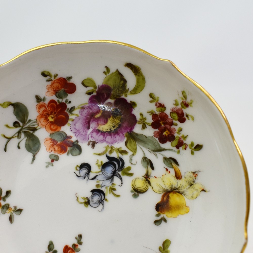 A white porcelain demitasse cup and matching saucer painted with polychrome floral sprays and finished with gold gilded scalloped edges. View IX
