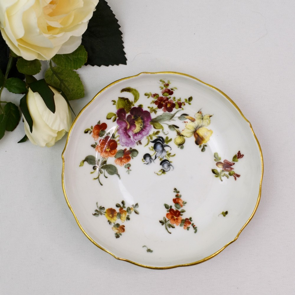 A white porcelain demitasse cup and matching saucer painted with polychrome floral sprays and finished with gold gilded scalloped edges. View X