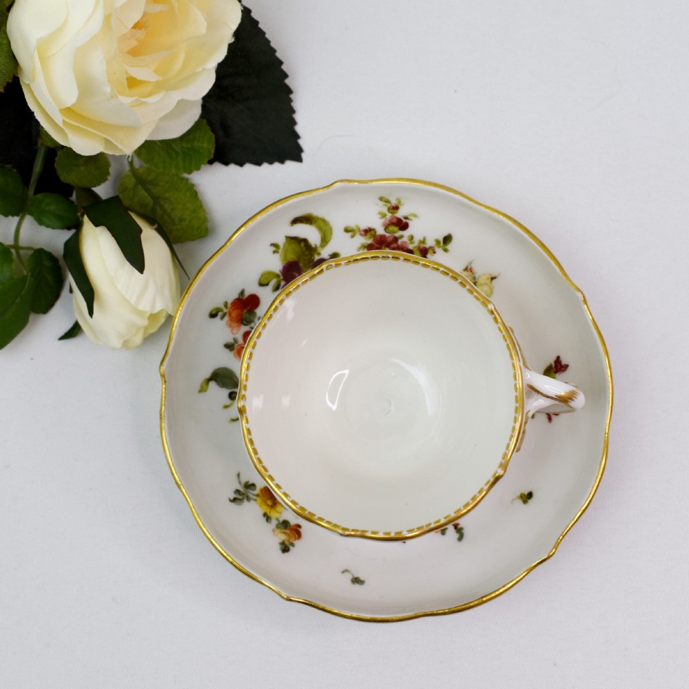 A white porcelain demitasse cup and matching saucer painted with polychrome floral sprays and finished with gold gilded scalloped edges. View XI