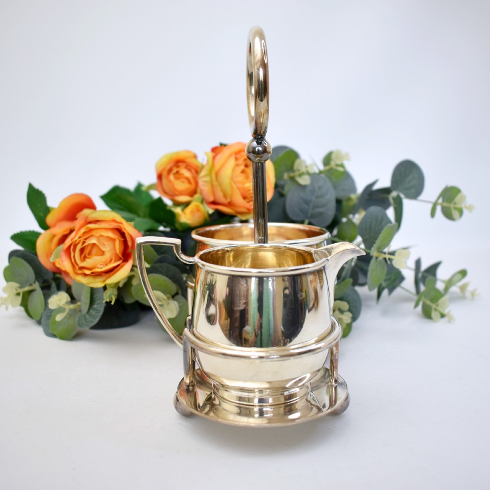 An Edwardian silver-plated cream jug and sugar bowl set held within a fitted stand featuring a central ring handle and ball feet. View III