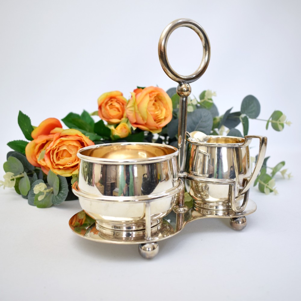 An Edwardian silver-plated cream jug and sugar bowl set held within a fitted stand featuring a central ring handle and ball feet. View VI