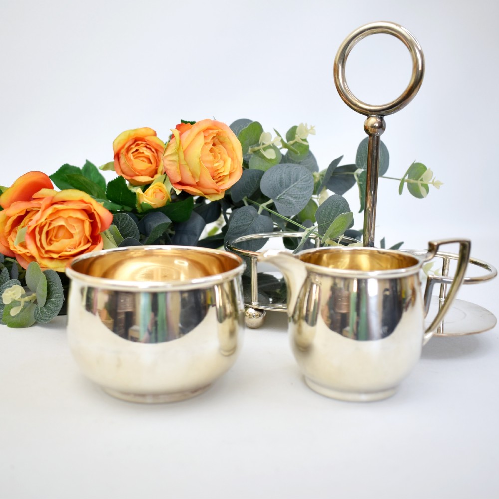 An Edwardian silver-plated cream jug and sugar bowl set held within a fitted stand featuring a central ring handle and ball feet. View VII