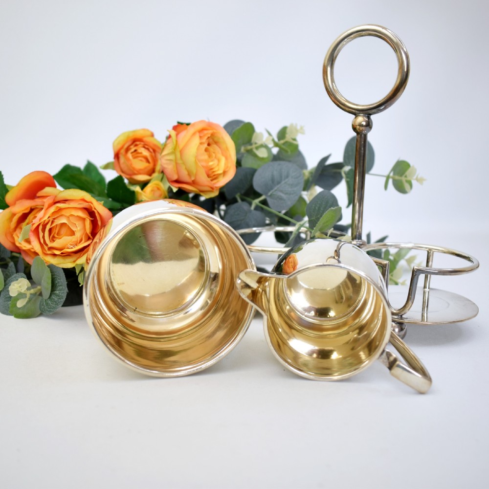 An Edwardian silver-plated cream jug and sugar bowl set held within a fitted stand featuring a central ring handle and ball feet. View VIII