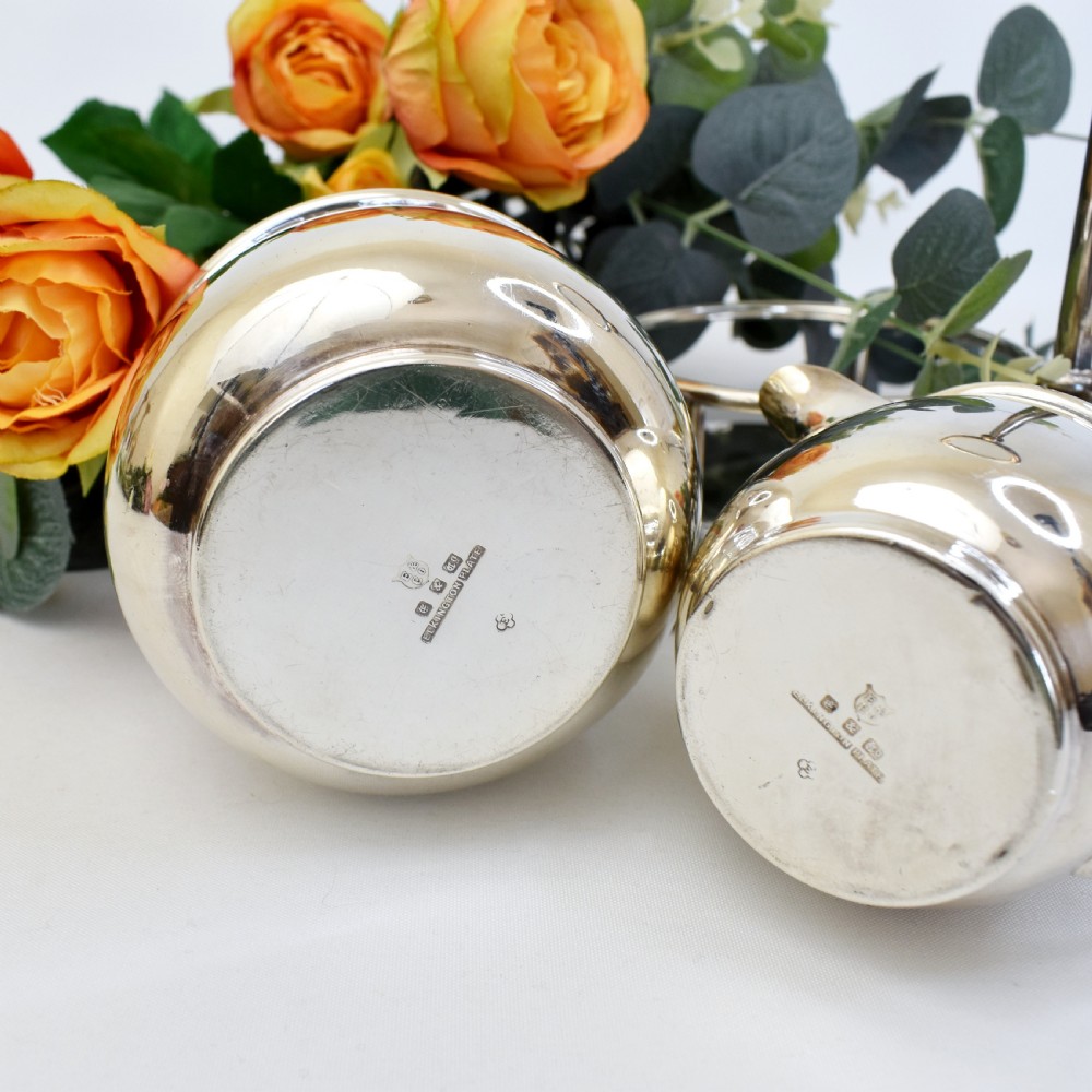 An Edwardian silver-plated cream jug and sugar bowl set held within a fitted stand featuring a central ring handle and ball feet. View IX
