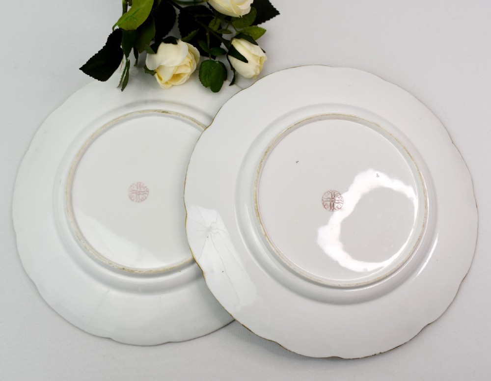 A pair of circular Victorian porcelain dessert plates featuring vibrant turquoise borders with gilded cartouches containing painted flowers and butterflies, with a central spray of pink roses on a white field. View XII