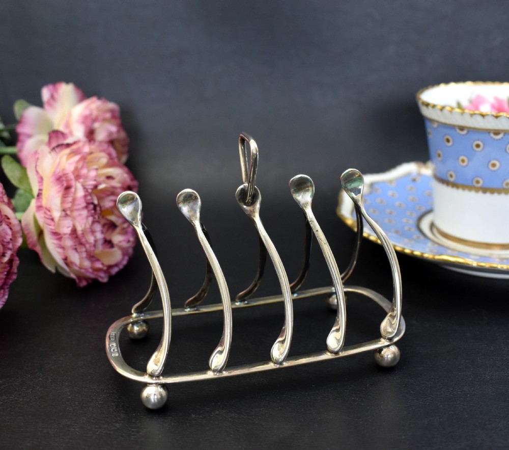 An antique sterling silver four-slot toast rack featuring wishbone-shaped dividers, a central loop handle, and ball feet.
