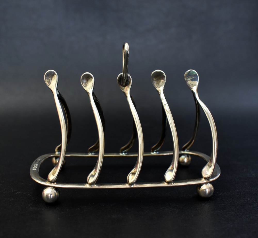 An antique sterling silver four-slot toast rack featuring wishbone-shaped dividers, a central loop handle, and ball feet. View II