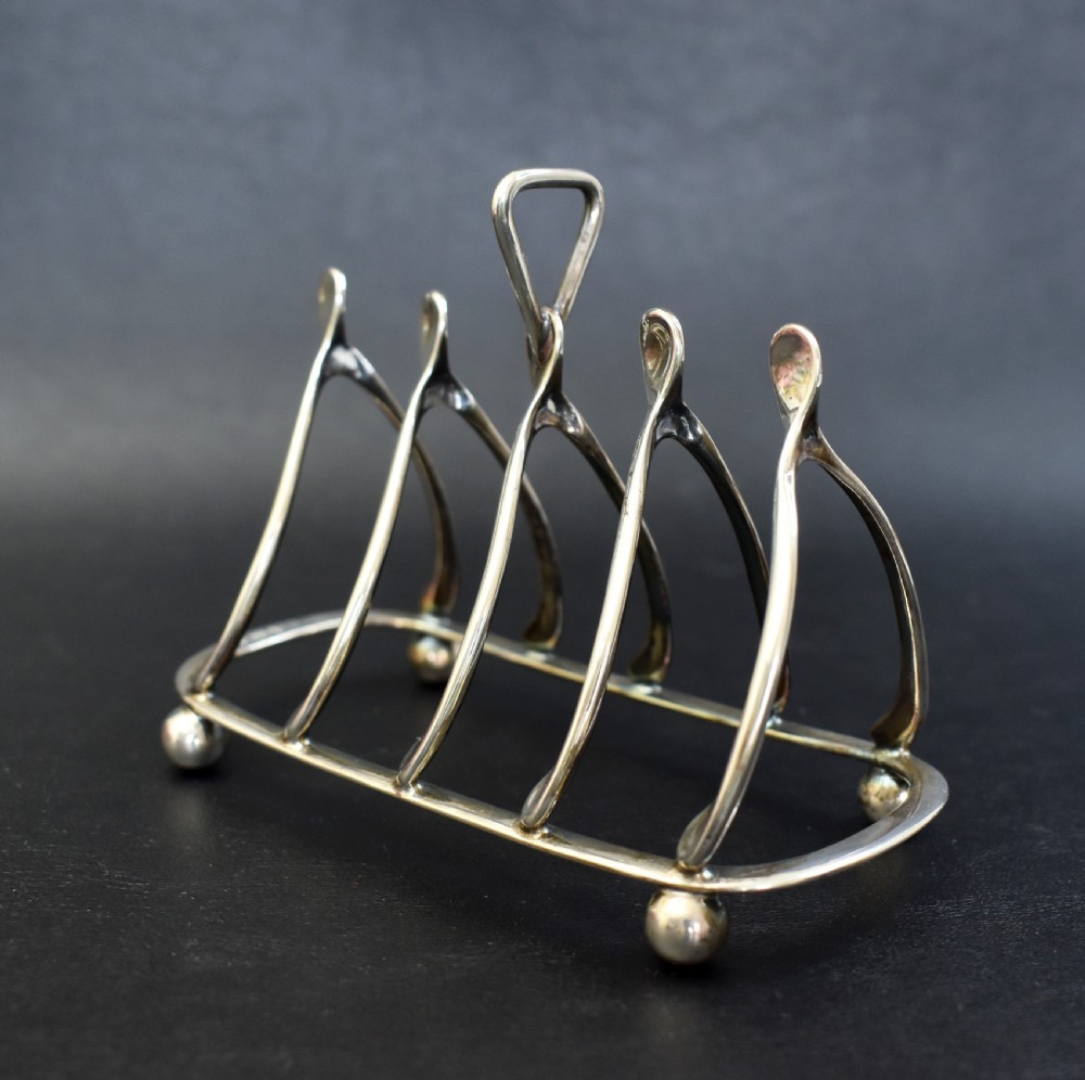 An antique sterling silver four-slot toast rack featuring wishbone-shaped dividers, a central loop handle, and ball feet. View III