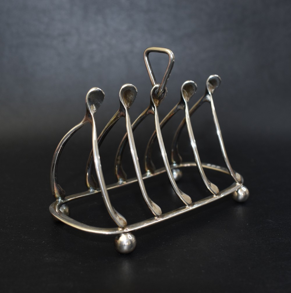 An antique sterling silver four-slot toast rack featuring wishbone-shaped dividers, a central loop handle, and ball feet. View V