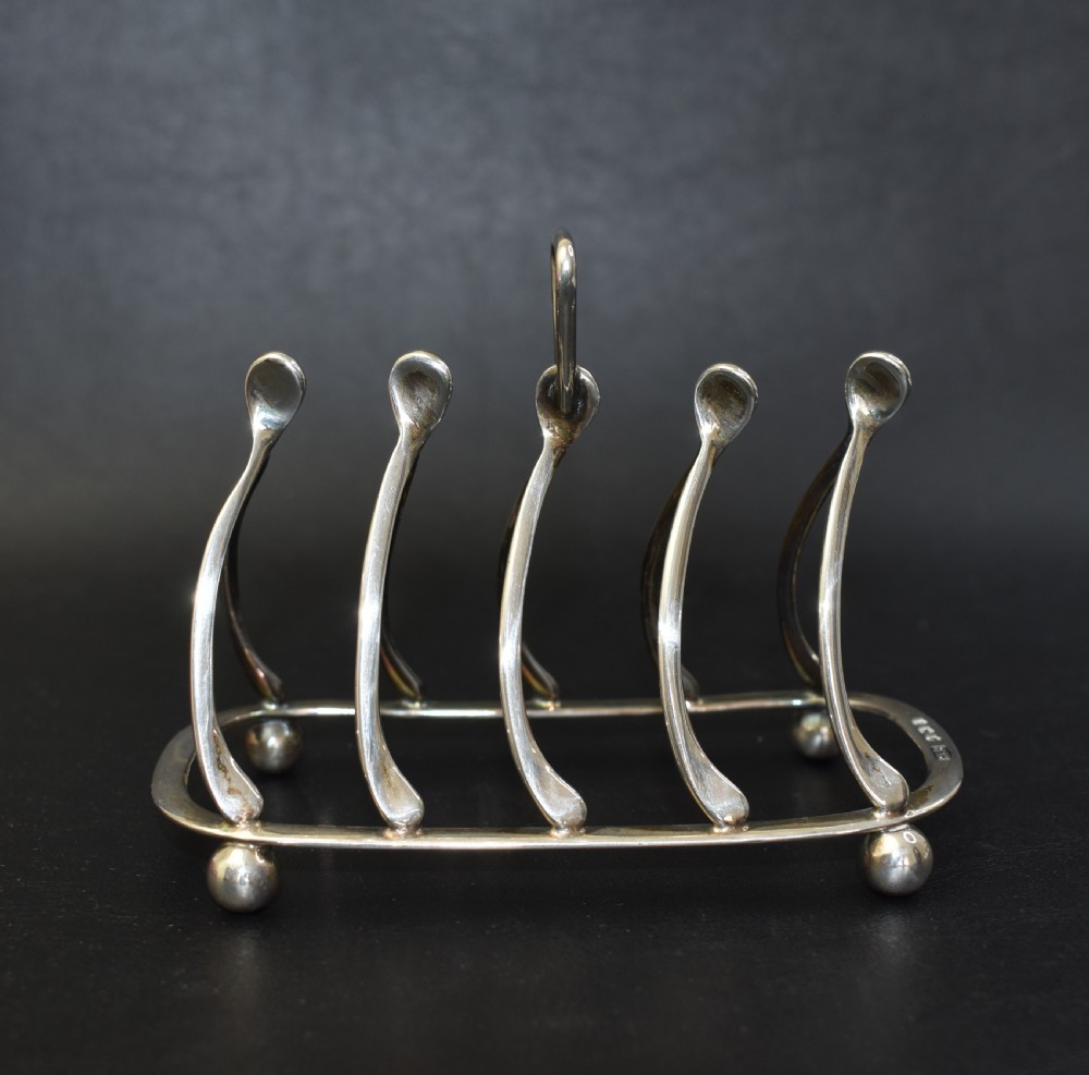 An antique sterling silver four-slot toast rack featuring wishbone-shaped dividers, a central loop handle, and ball feet. View VI