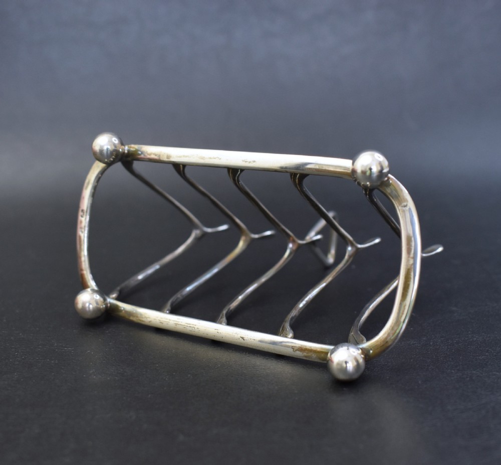 An antique sterling silver four-slot toast rack featuring wishbone-shaped dividers, a central loop handle, and ball feet. View IX