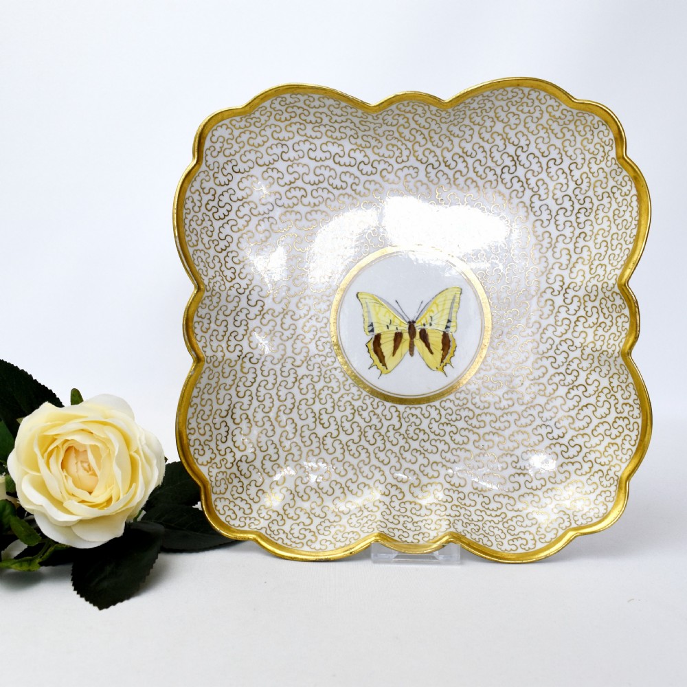 A square lobed white porcelain dish decorated with intricate gold scrollwork around a central hand-painted yellow butterfly medallion. View V