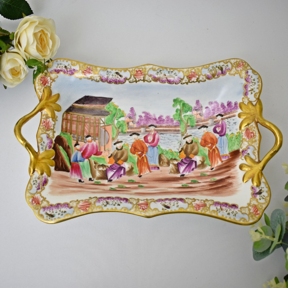 A Regency-era rectangular Swansea porcelain comport featuring gilded twin handles, a shaped border, and a polychrome hand-painted Mandarin Chinoiserie landscape scene.