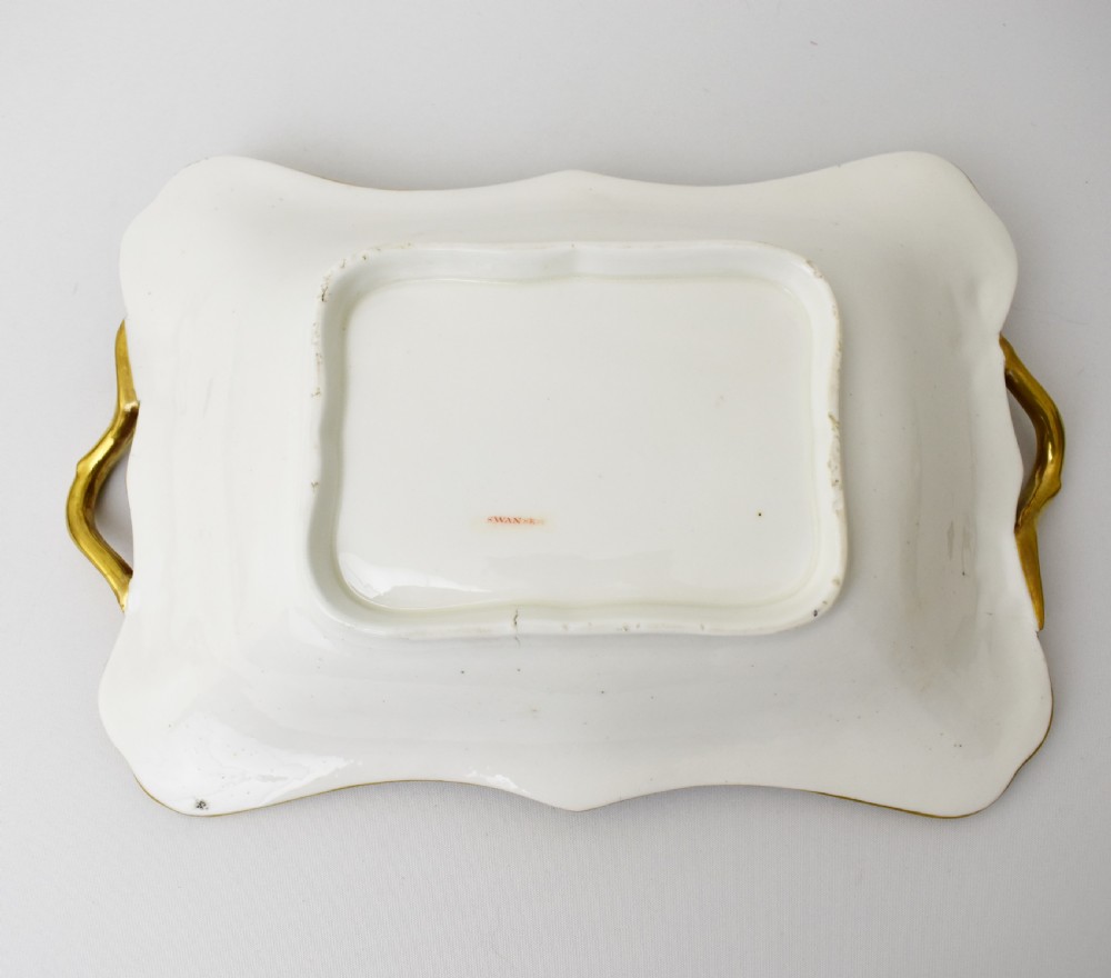 A Regency-era rectangular Swansea porcelain comport featuring gilded twin handles, a shaped border, and a polychrome hand-painted Mandarin Chinoiserie landscape scene. View X