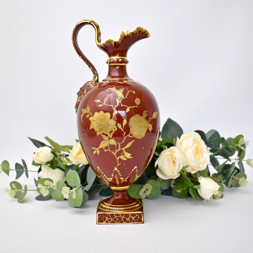 A Victorian Royal Crown Derby porcelain ewer with a terracotta brown ground, single loop handle, flared spout, and raised gold floral gilding on a square pedestal base. View III