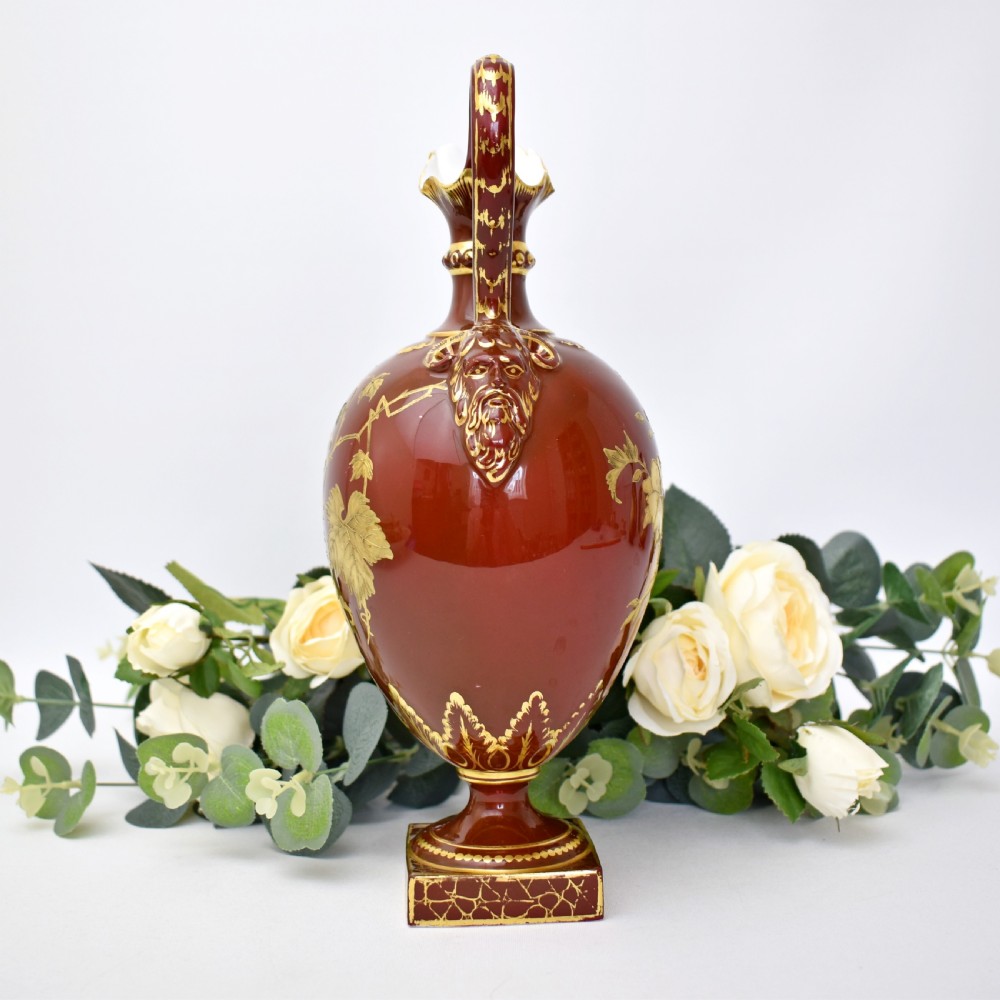 A Victorian Royal Crown Derby porcelain ewer with a terracotta brown ground, single loop handle, flared spout, and raised gold floral gilding on a square pedestal base. View IV