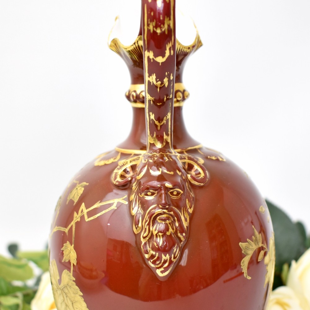 A Victorian Royal Crown Derby porcelain ewer with a terracotta brown ground, single loop handle, flared spout, and raised gold floral gilding on a square pedestal base. View V