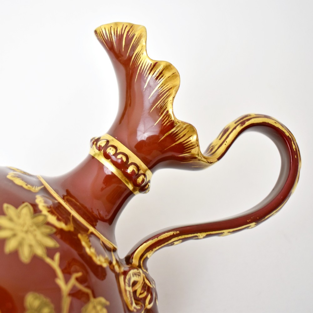A Victorian Royal Crown Derby porcelain ewer with a terracotta brown ground, single loop handle, flared spout, and raised gold floral gilding on a square pedestal base. View IX