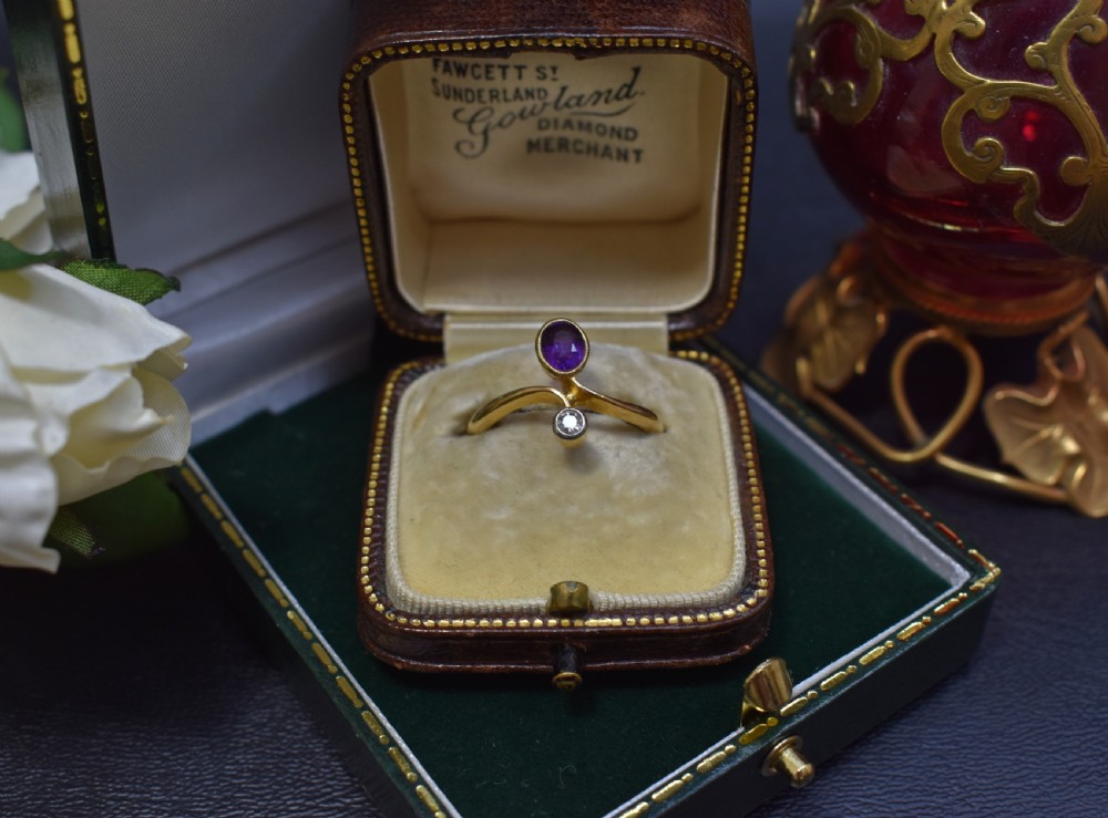 An Art Nouveau 18ct yellow gold ring featuring an oval bezel-set purple amethyst gemstone with a sweeping band and a small drop-set diamond accent. View II