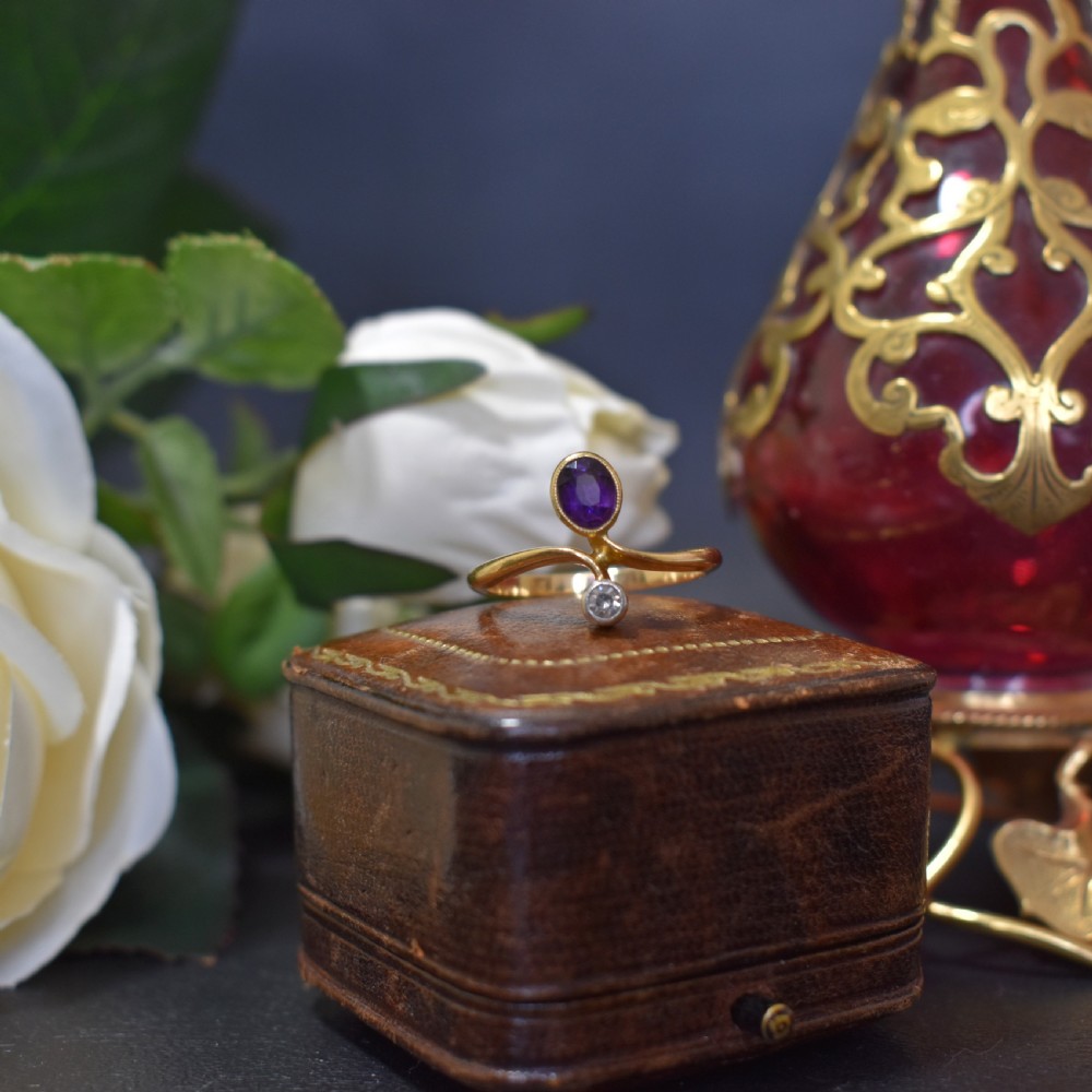 An Art Nouveau 18ct yellow gold ring featuring an oval bezel-set purple amethyst gemstone with a sweeping band and a small drop-set diamond accent. View III