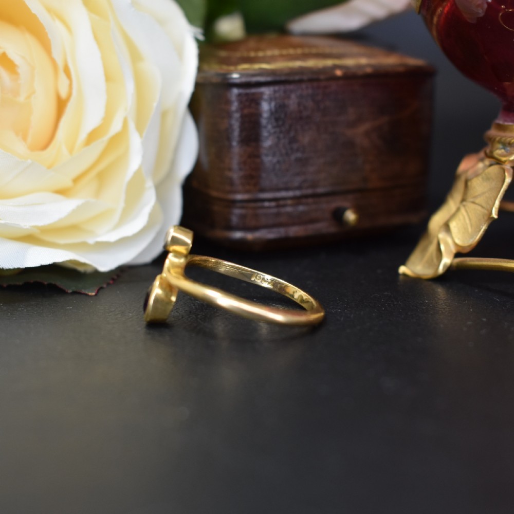 An Art Nouveau 18ct yellow gold ring featuring an oval bezel-set purple amethyst gemstone with a sweeping band and a small drop-set diamond accent. View IX