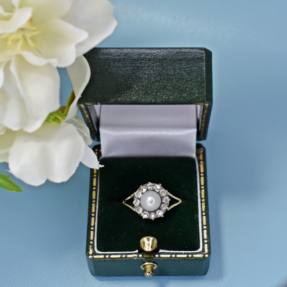 An Edwardian 18ct yellow gold cluster ring featuring a central white pearl surrounded by a halo of old cut diamonds with split shoulders. View IX