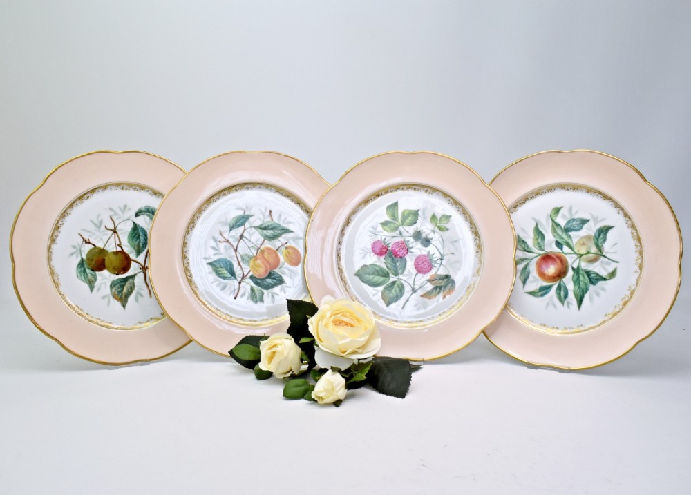 A set of four circular Russian porcelain plates decorated with hand-painted botanical fruit motifs, blush pink borders, and scalloped gilded rims.