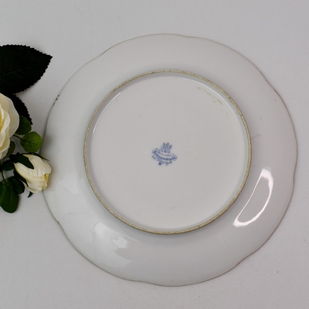 A set of four circular Russian porcelain plates decorated with hand-painted botanical fruit motifs, blush pink borders, and scalloped gilded rims. View X