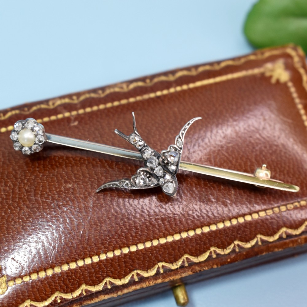 An Edwardian 15ct gold bar brooch featuring a silver-topped swallow in flight set with rose-cut diamonds beside a pearl cluster. View II