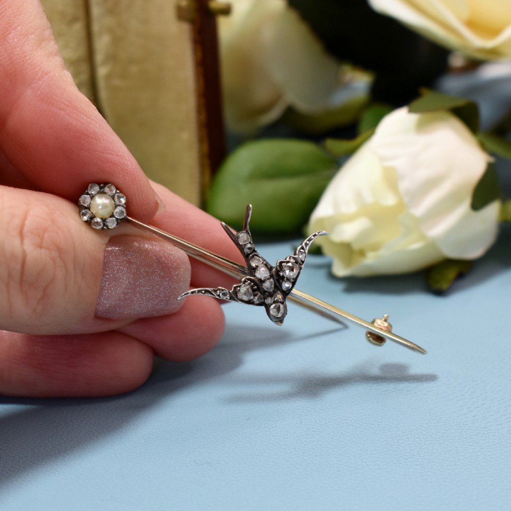 An Edwardian 15ct gold bar brooch featuring a silver-topped swallow in flight set with rose-cut diamonds beside a pearl cluster. View VI