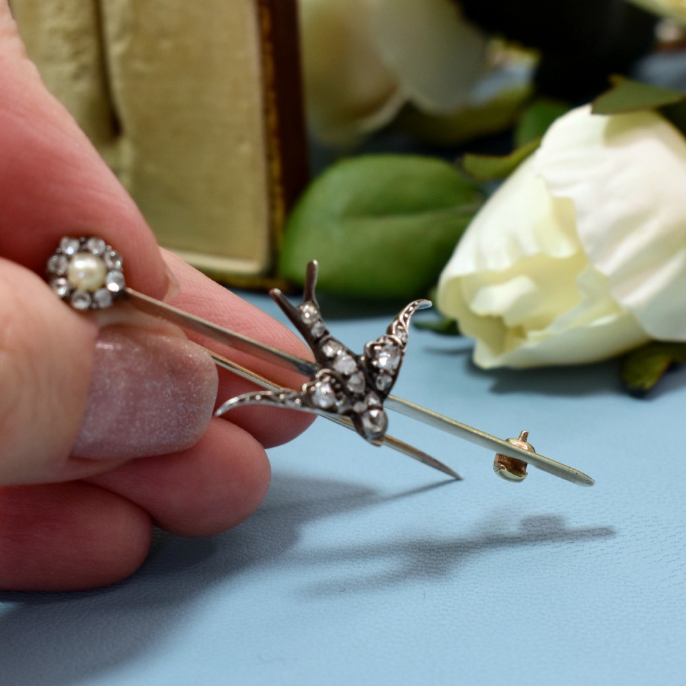 An Edwardian 15ct gold bar brooch featuring a silver-topped swallow in flight set with rose-cut diamonds beside a pearl cluster. View VII