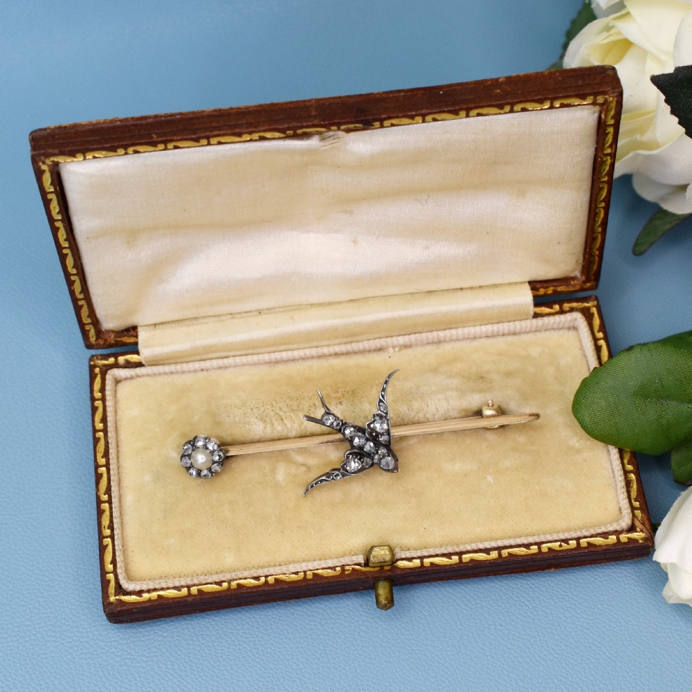 An Edwardian 15ct gold bar brooch featuring a silver-topped swallow in flight set with rose-cut diamonds beside a pearl cluster. View X