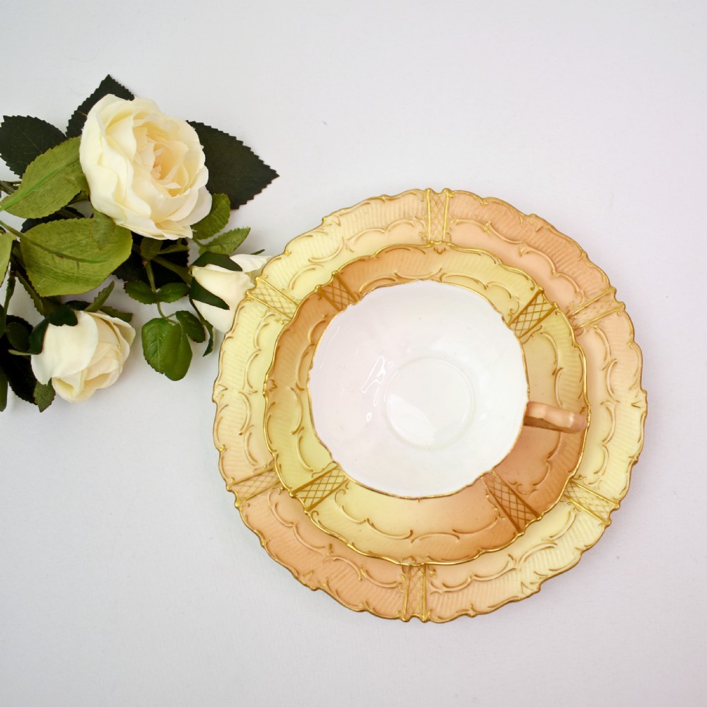 An Edwardian Royal Worcester tea trio featuring a teacup, saucer, and side plate rendered in gradient blush ivory porcelain with gilded scalloped edges. View III