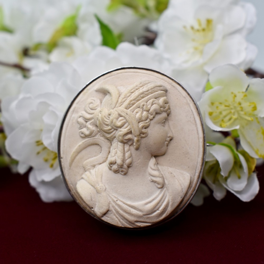 An oval Victorian lava stone brooch featuring a carved high-relief profile portrait of Demeter enclosed in a silver bezel setting.