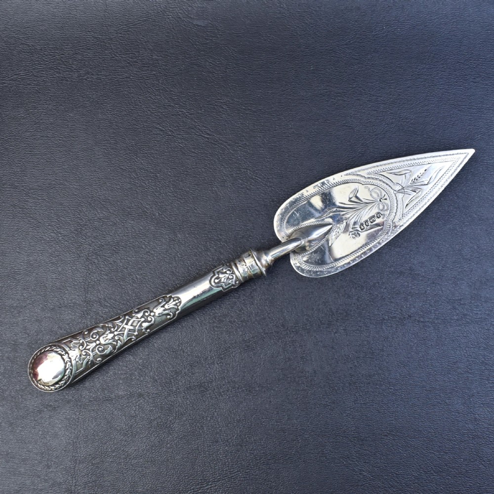 A Victorian sterling silver pastry server with a pointed trowel-shaped blade engraved with floral motifs and an ornate relief handle.