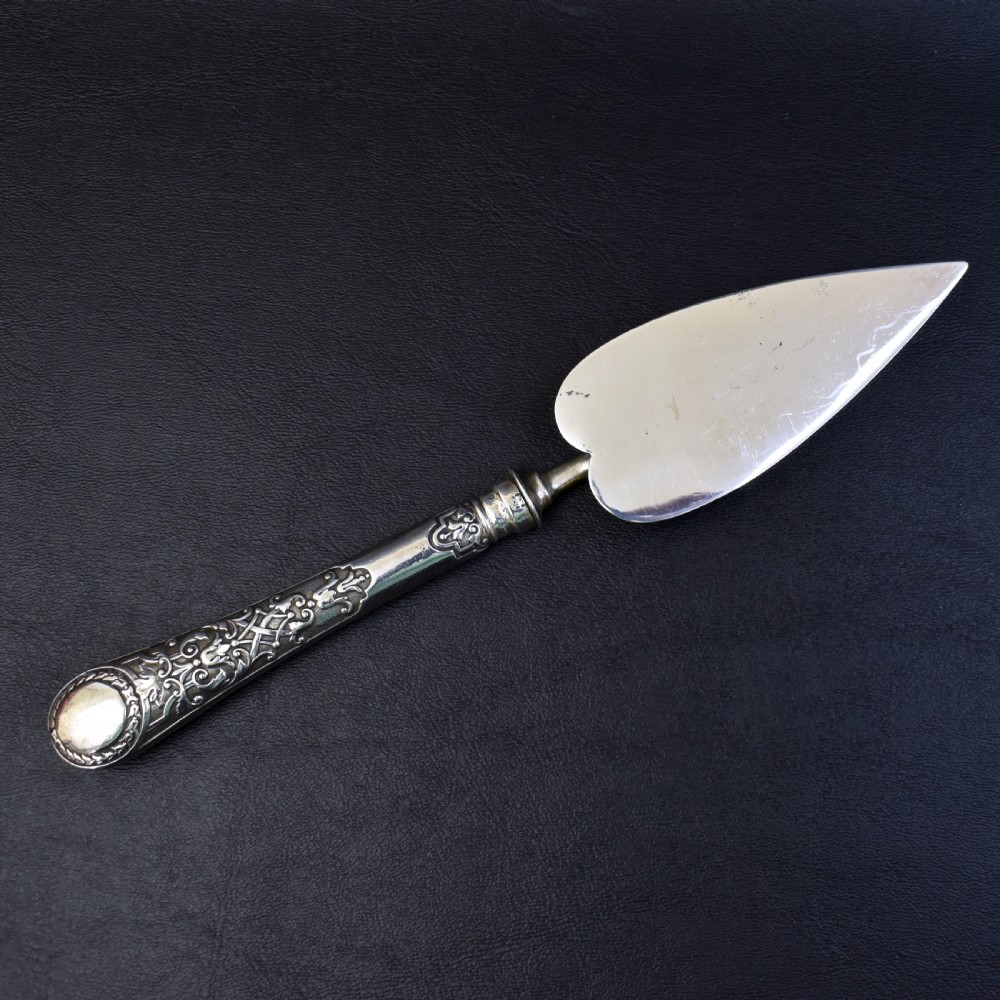 A Victorian sterling silver pastry server with a pointed trowel-shaped blade engraved with floral motifs and an ornate relief handle. View VI